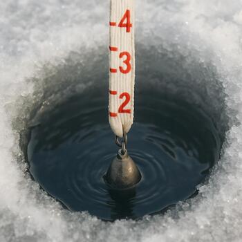 Measuring line disappearing into a drilled ice hole to check depth
